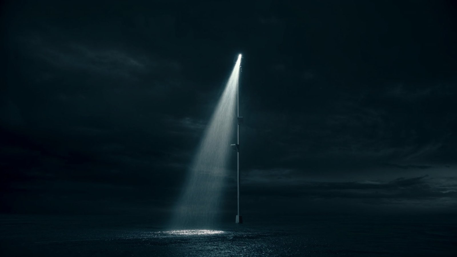 A single floodlight cutting one hard cone of light through falling rain