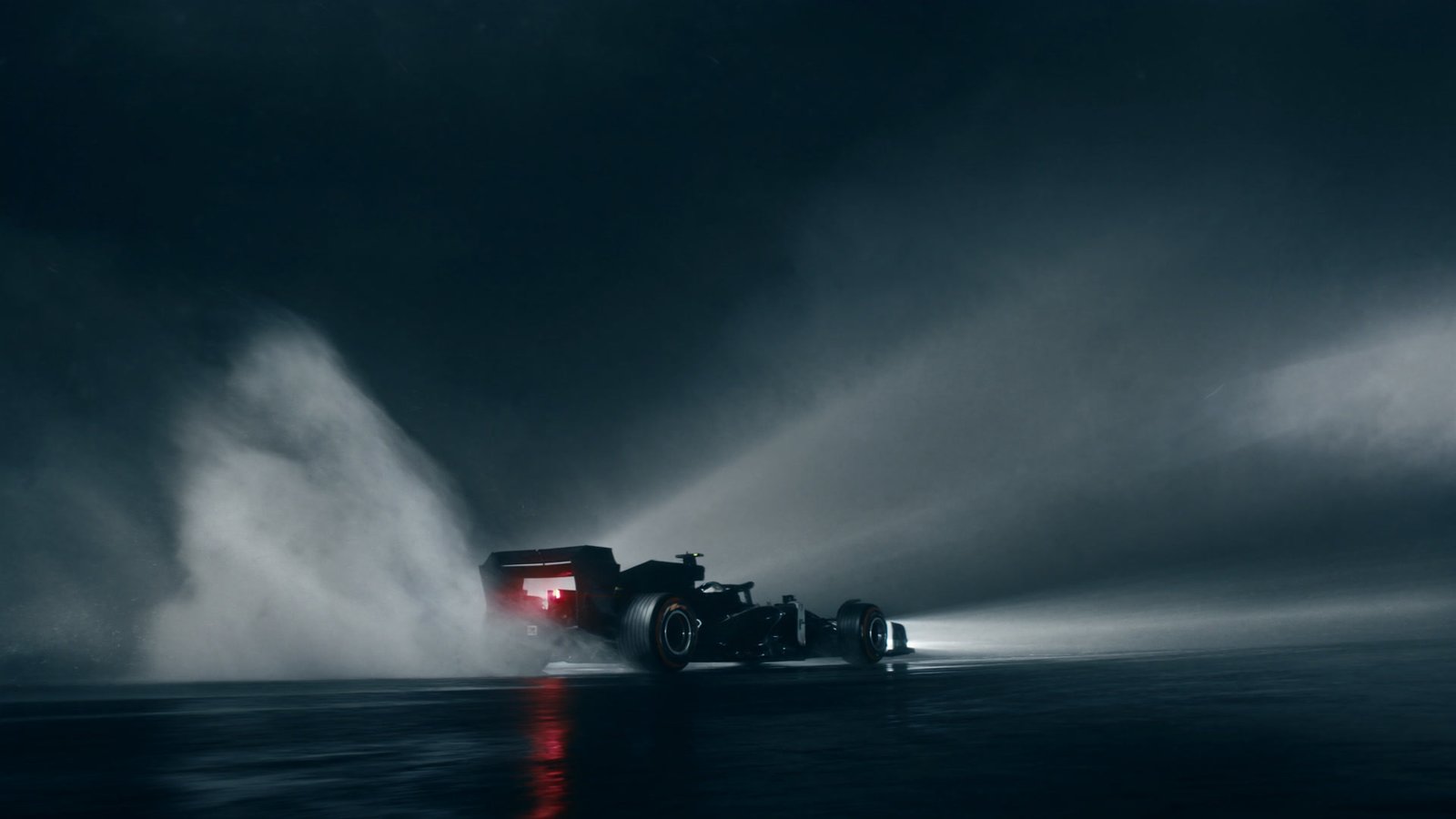 An open wheel car throwing spray into the floodlights on a soaked circuit at night